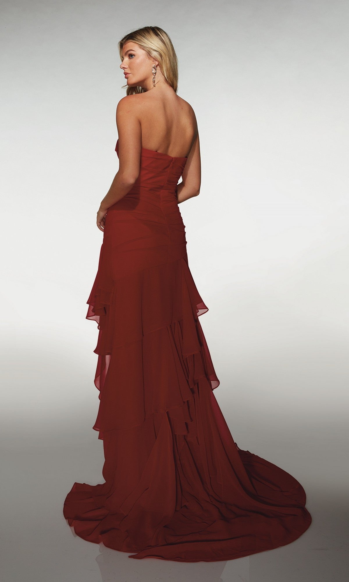 A woman models the Alyce 62153 long formal dress, a strapless dark red gown with ruffled details, standing against a plain light background and looking over her shoulder.